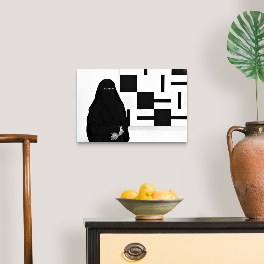 A traditional room featuring A woman wearing a black niqab stands next to a painting made of black and white squares.