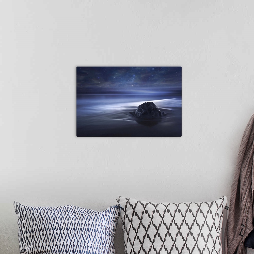 A bohemian room featuring A rock on the beach in sand which appears smooth, under a starry night sky.