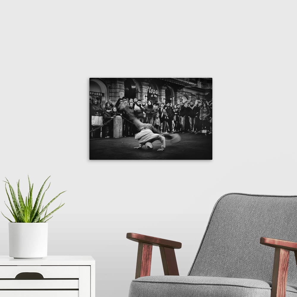 A modern room featuring A breakdancer spins on their head while performing in the street, while onlookers watch.