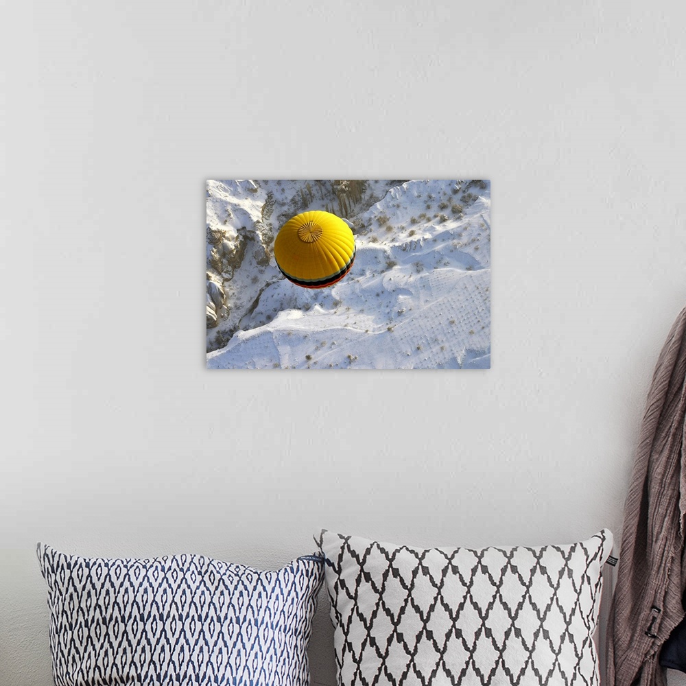 A bohemian room featuring A yellow hot air balloon floats above the snow covered landscape of Cappadocia, Turkey.