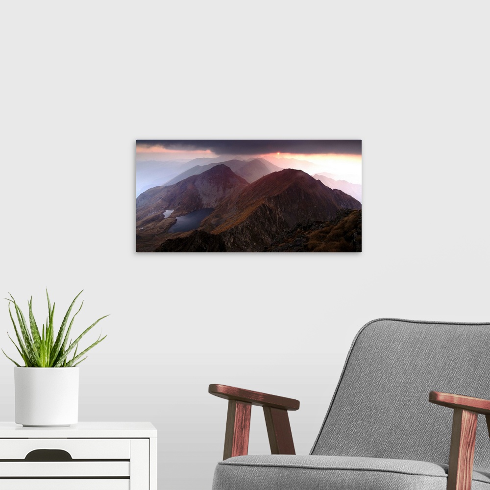 A modern room featuring Sunset just visible under dark clouds over the Fagaras Mountains in Romania.