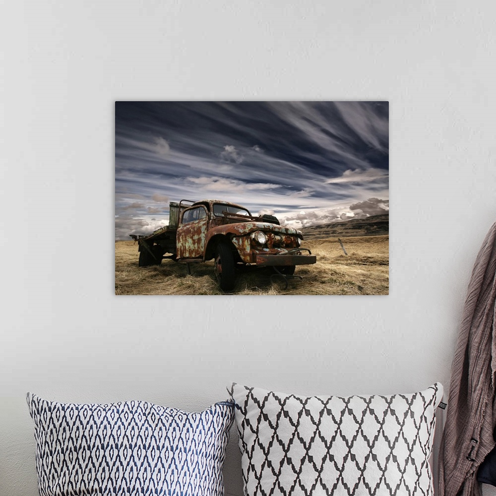 A bohemian room featuring An old rusted truck sits unused in a field under a sky with dramatic clouds.