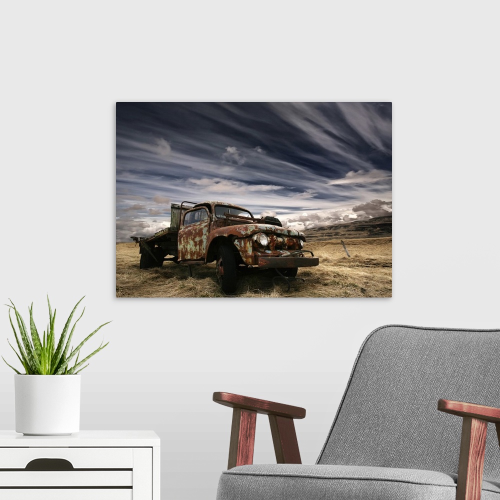 A modern room featuring An old rusted truck sits unused in a field under a sky with dramatic clouds.