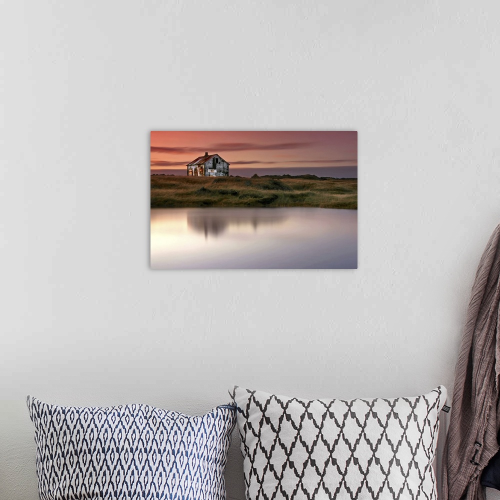 A bohemian room featuring An abandoned farm house on the grassy shore by a lake in Iceland, at sunrise.