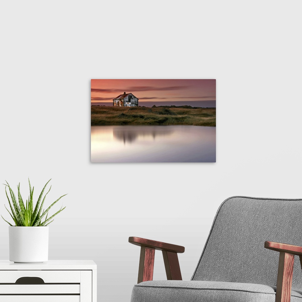 A modern room featuring An abandoned farm house on the grassy shore by a lake in Iceland, at sunrise.