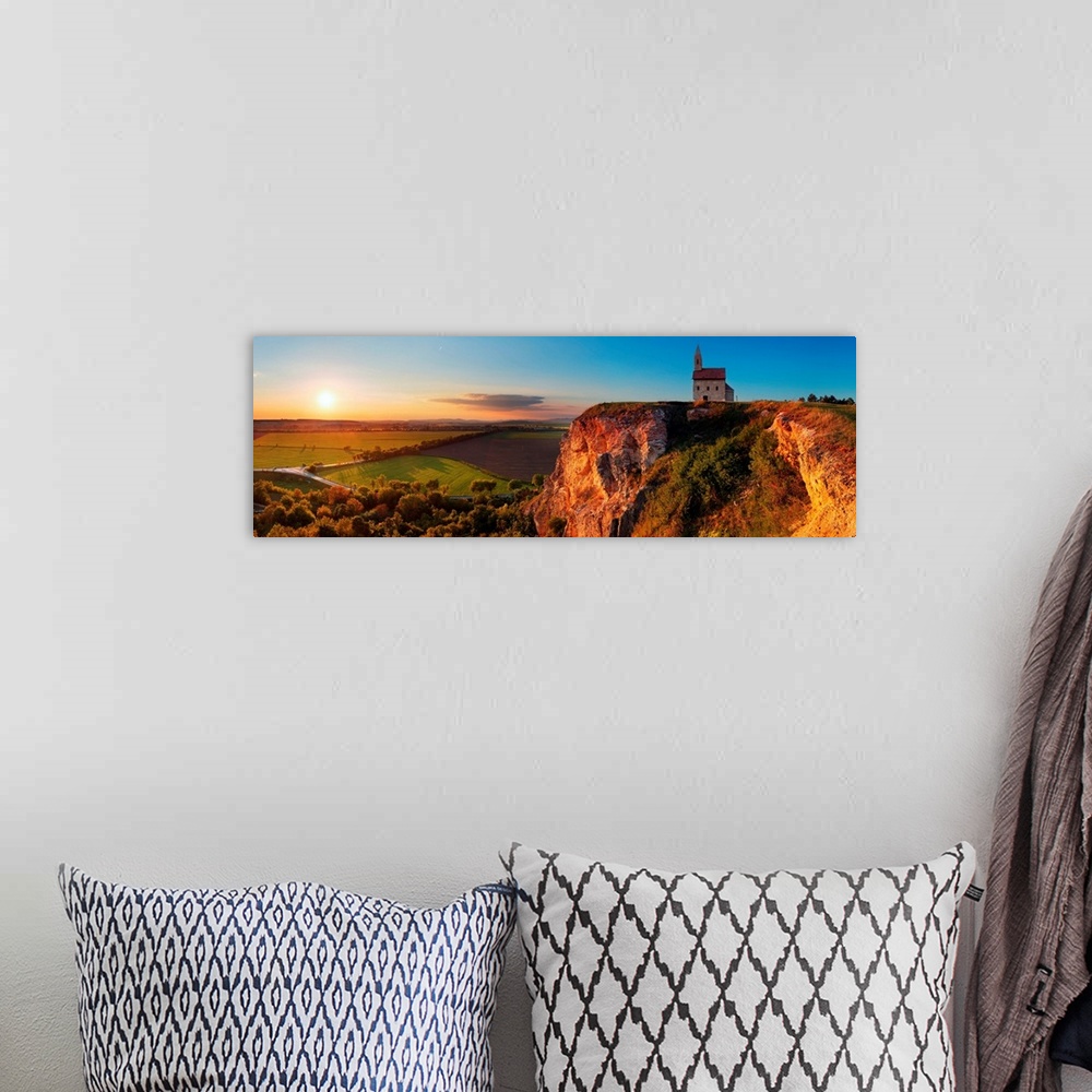 A bohemian room featuring Panoramic image of a church on a cliff overlooking a village in Slovakia at sunset.