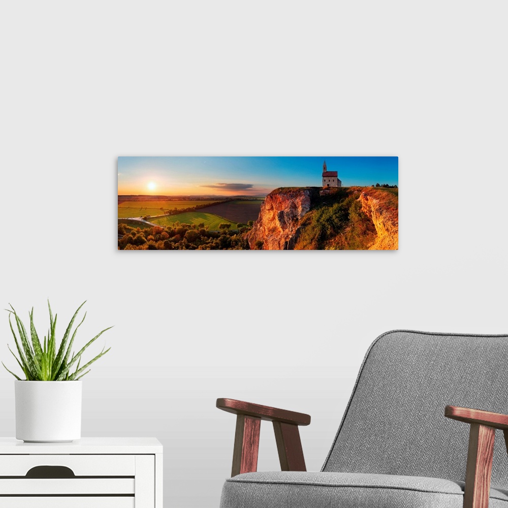 A modern room featuring Panoramic image of a church on a cliff overlooking a village in Slovakia at sunset.