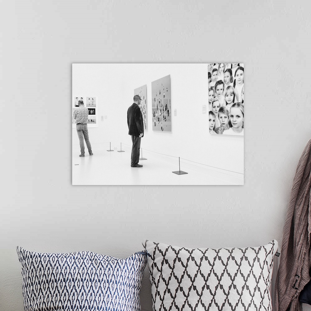 A bohemian room featuring A man in an art gallery looks at figurative artwork on the wall.