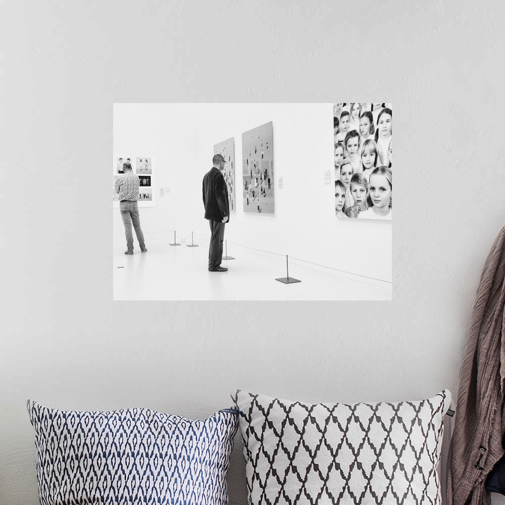 A bohemian room featuring A man in an art gallery looks at figurative artwork on the wall.