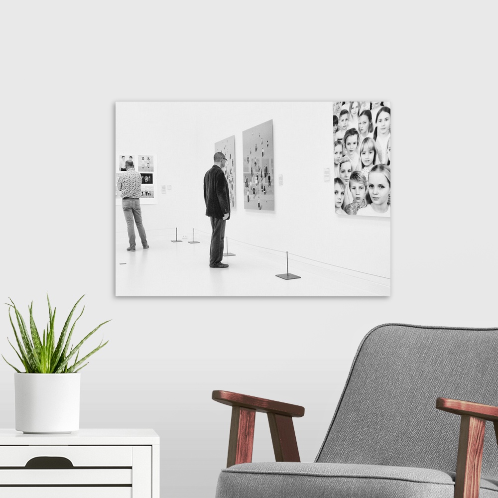 A modern room featuring A man in an art gallery looks at figurative artwork on the wall.