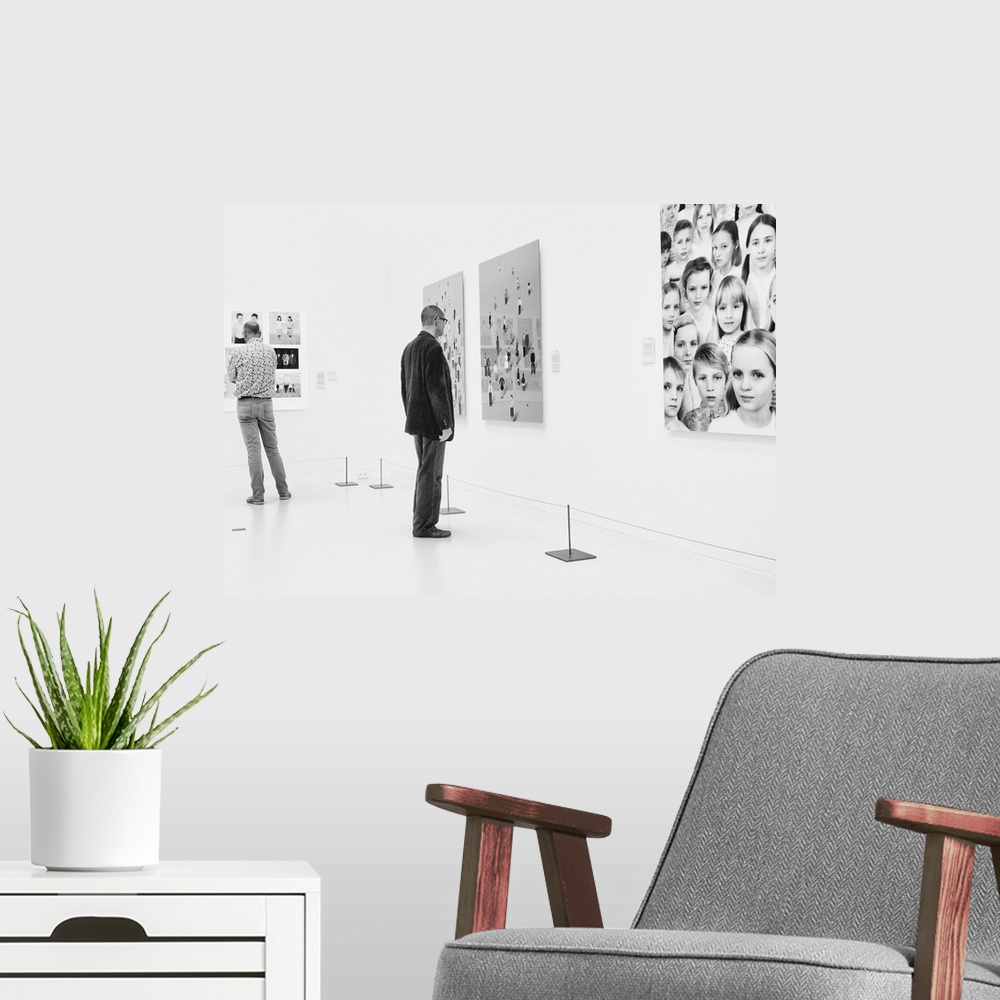 A modern room featuring A man in an art gallery looks at figurative artwork on the wall.