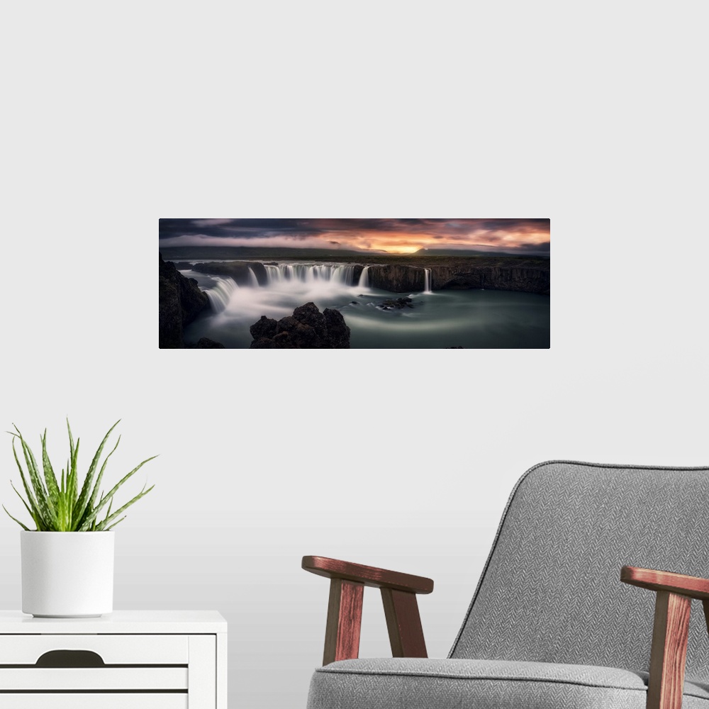 A modern room featuring An intense photograph of a waterfall curtain with mountains and dramatic clouds in the distance.