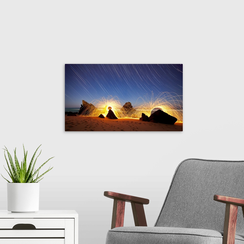 A modern room featuring Landscape photo of Praia da Adraga, Portugal at night with star trails in the sky and firework li...