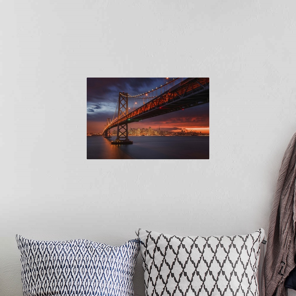 A bohemian room featuring The San Francisco bay bridge illuminated at night with a glowing sunset sky hanging over the city...