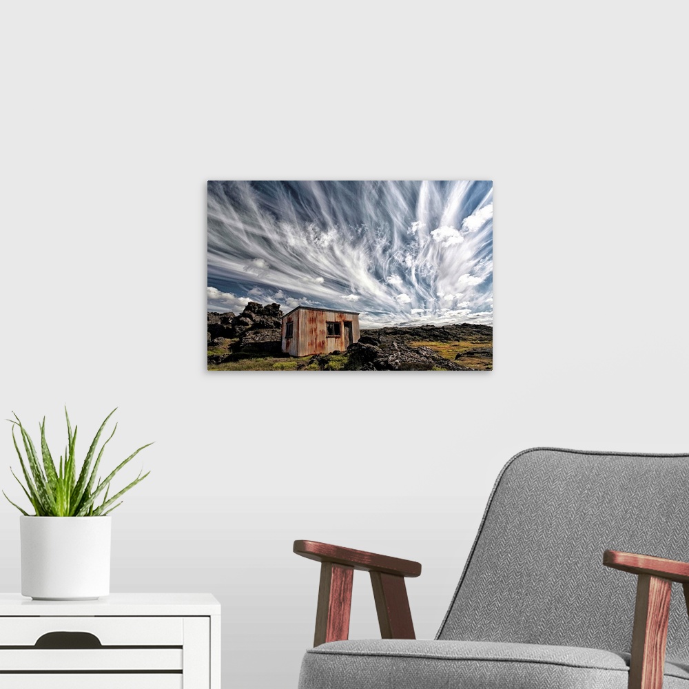 A modern room featuring A dramatic skyscape over a derelict shack in the Icelandic countryside.