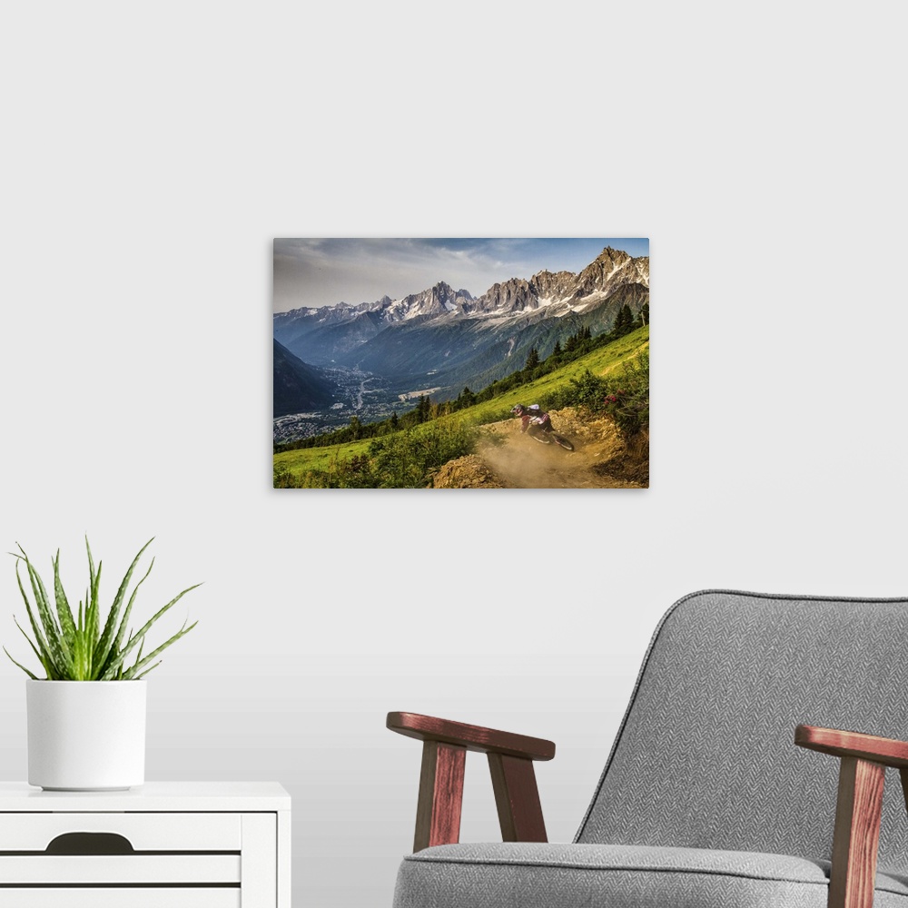 A modern room featuring A mountain biker kicking up dust from while riding a trail, with a spectacular mountain range in ...