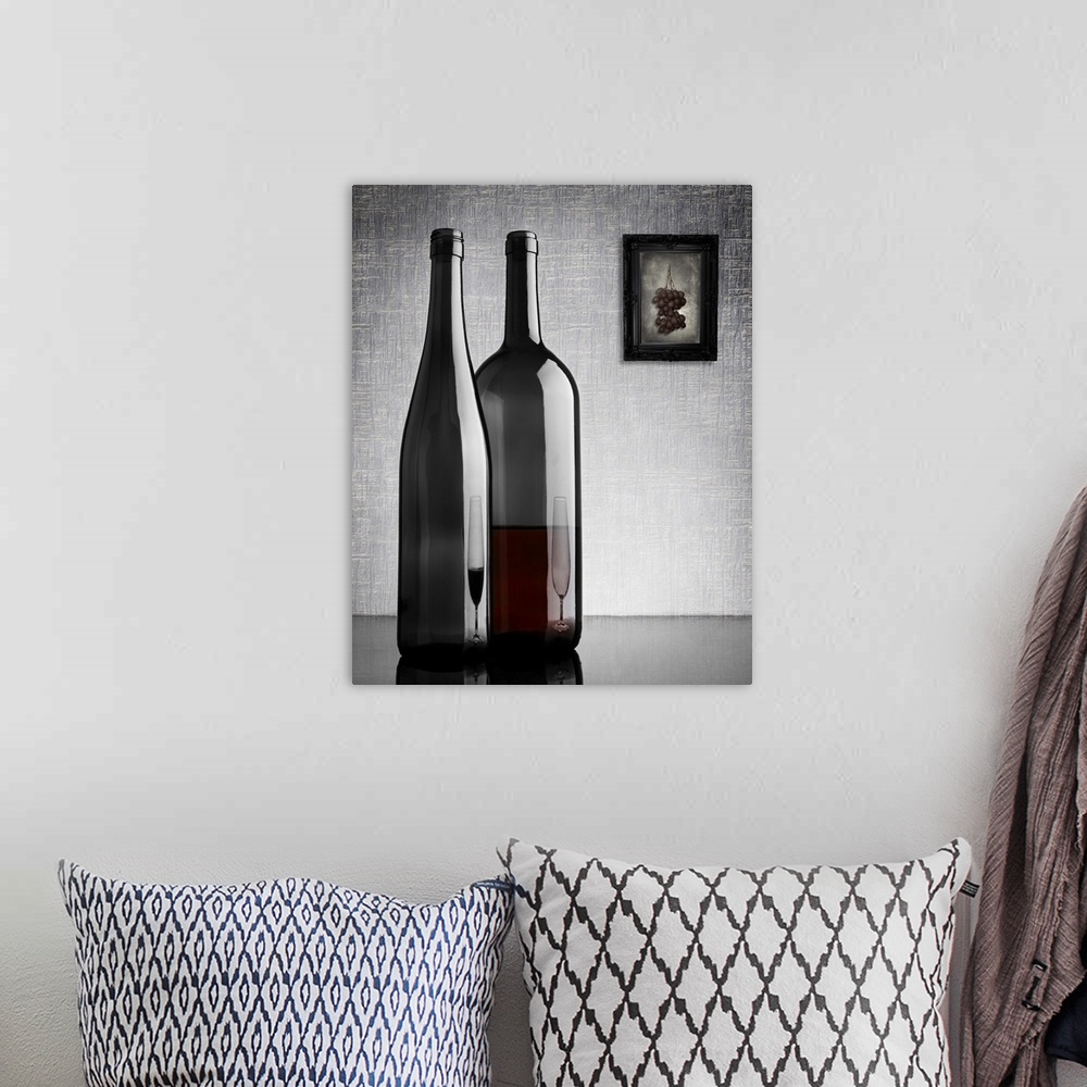 A bohemian room featuring Two glass wine bottles with reflections of glasses on them, and a framed image of grapes on the w...