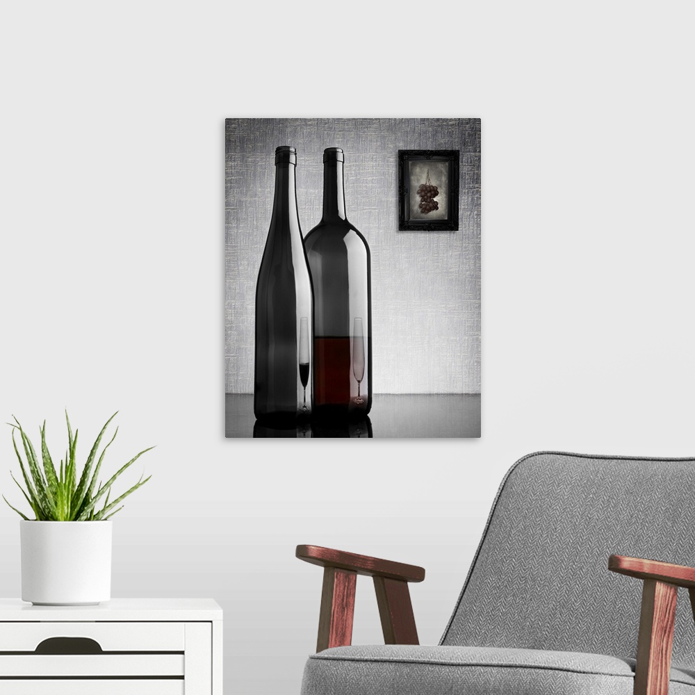 A modern room featuring Two glass wine bottles with reflections of glasses on them, and a framed image of grapes on the w...