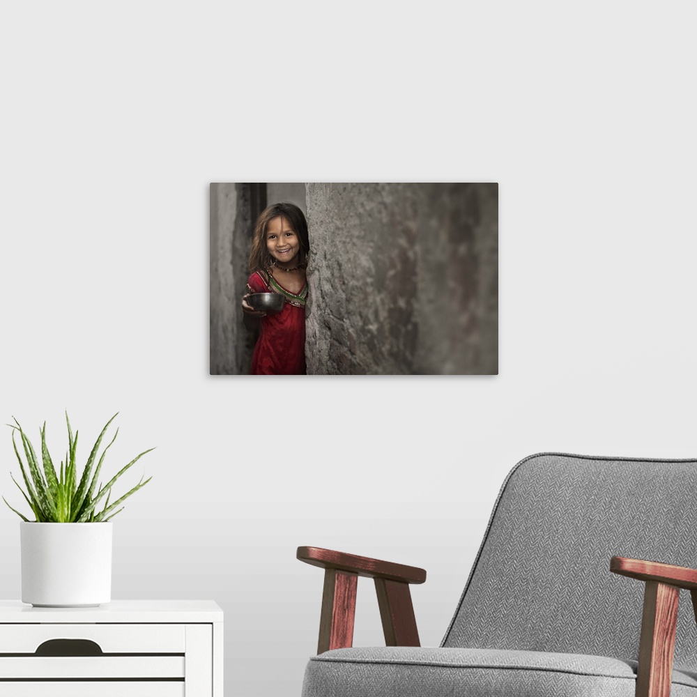 A modern room featuring A smiling little girl holding a bowl, standing beside a stone wall.