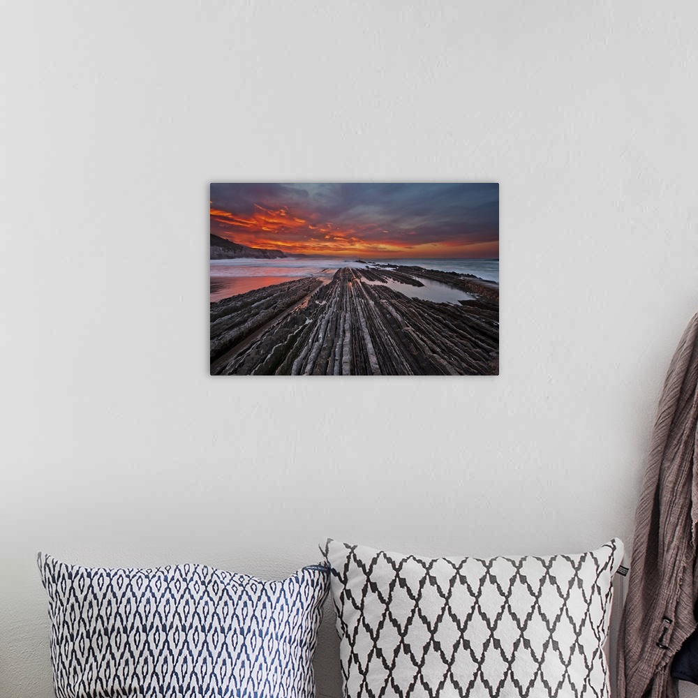 A bohemian room featuring Rocky textured landscape photograph with the ocean in the background and a firey sunset in Itzuru...