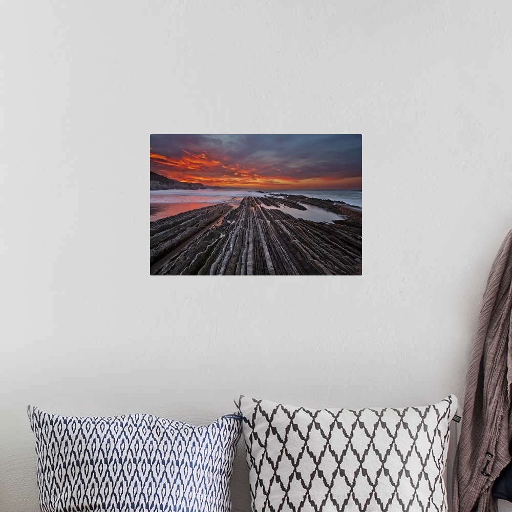 A bohemian room featuring Rocky textured landscape photograph with the ocean in the background and a firey sunset in Itzuru...
