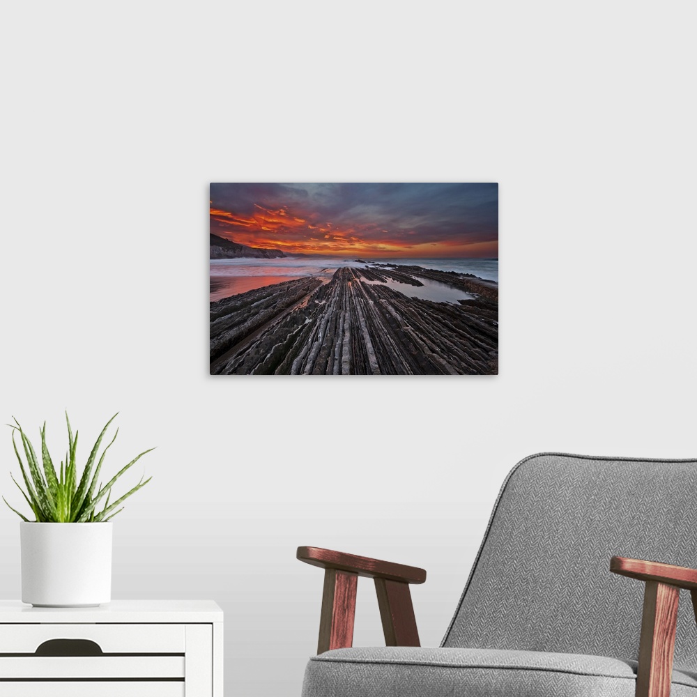 A modern room featuring Rocky textured landscape photograph with the ocean in the background and a firey sunset in Itzuru...