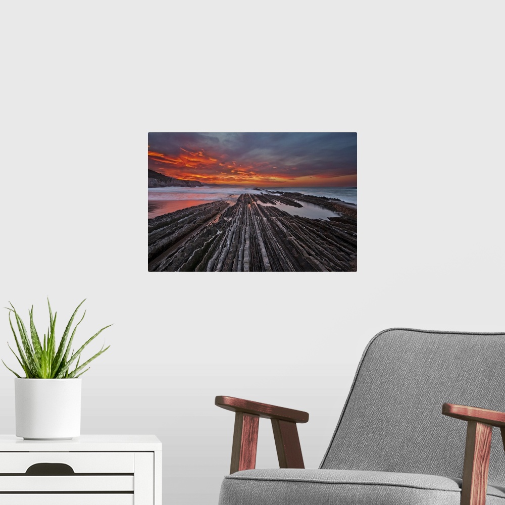 A modern room featuring Rocky textured landscape photograph with the ocean in the background and a firey sunset in Itzuru...