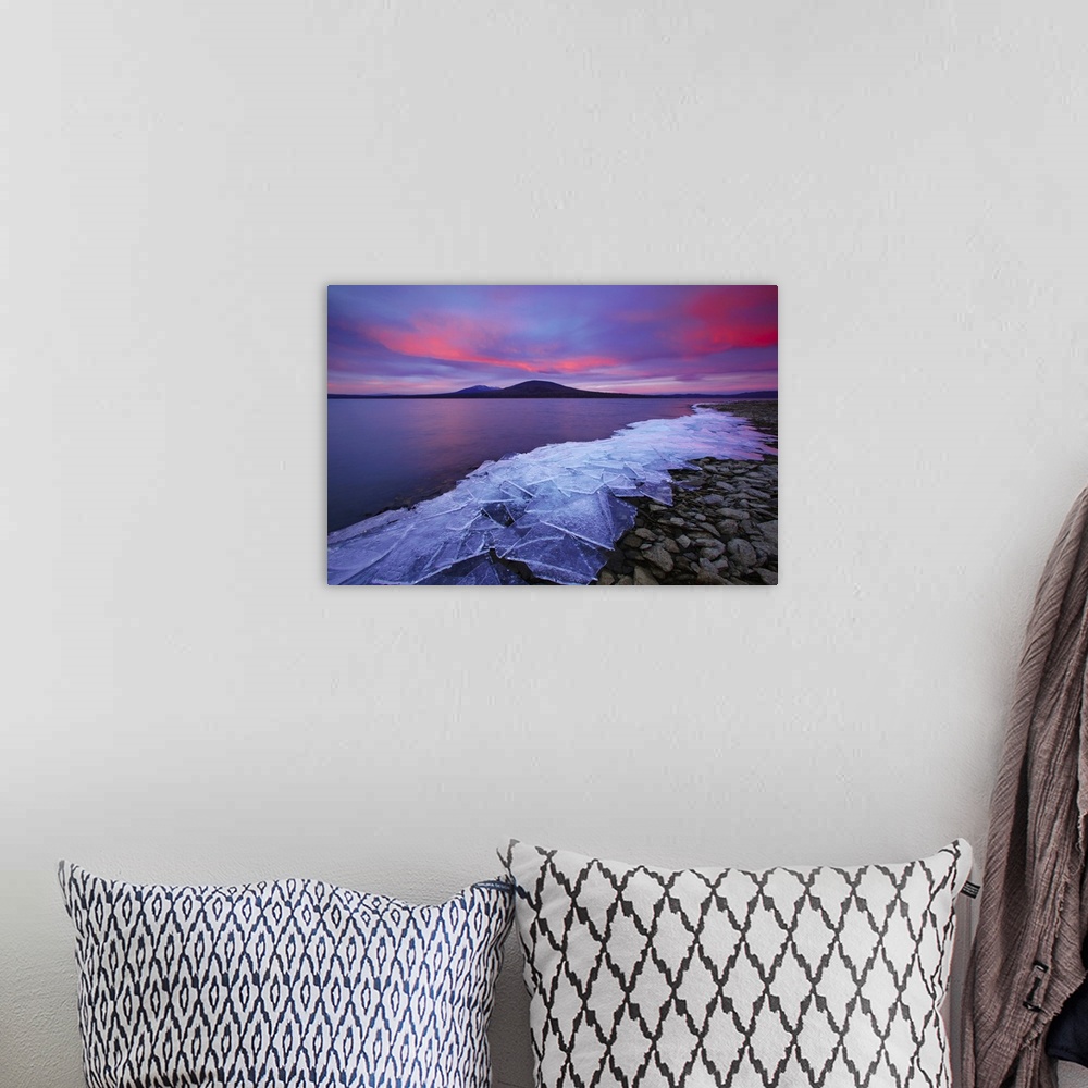 A bohemian room featuring Cracked ice sheets on a rocky shore at sunrise.