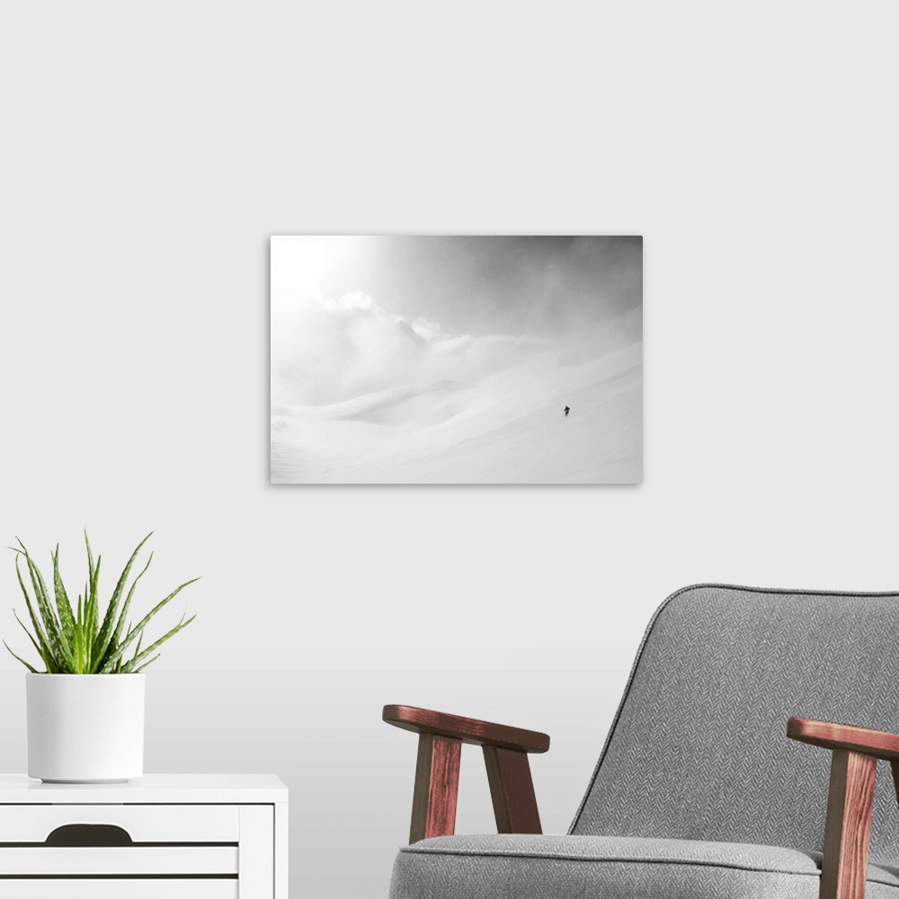 A modern room featuring White mountain landscape of snow and clouds with a lone skier made miniature by the vast expanse.