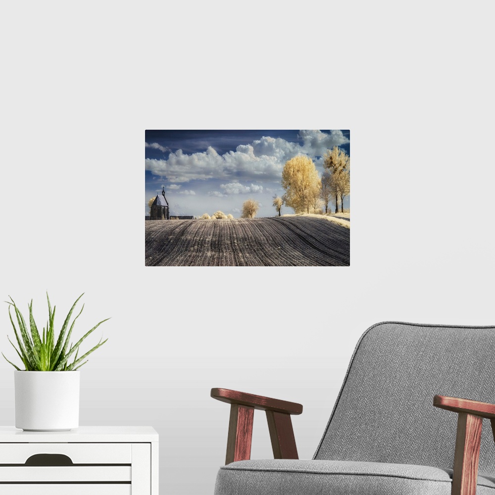 A modern room featuring Infrared image of a tilled field in the countryside in Poland, with a church and trees.