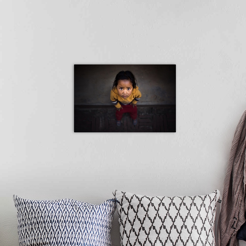 A bohemian room featuring A young Nepalese girl looking up with large dark eyes.