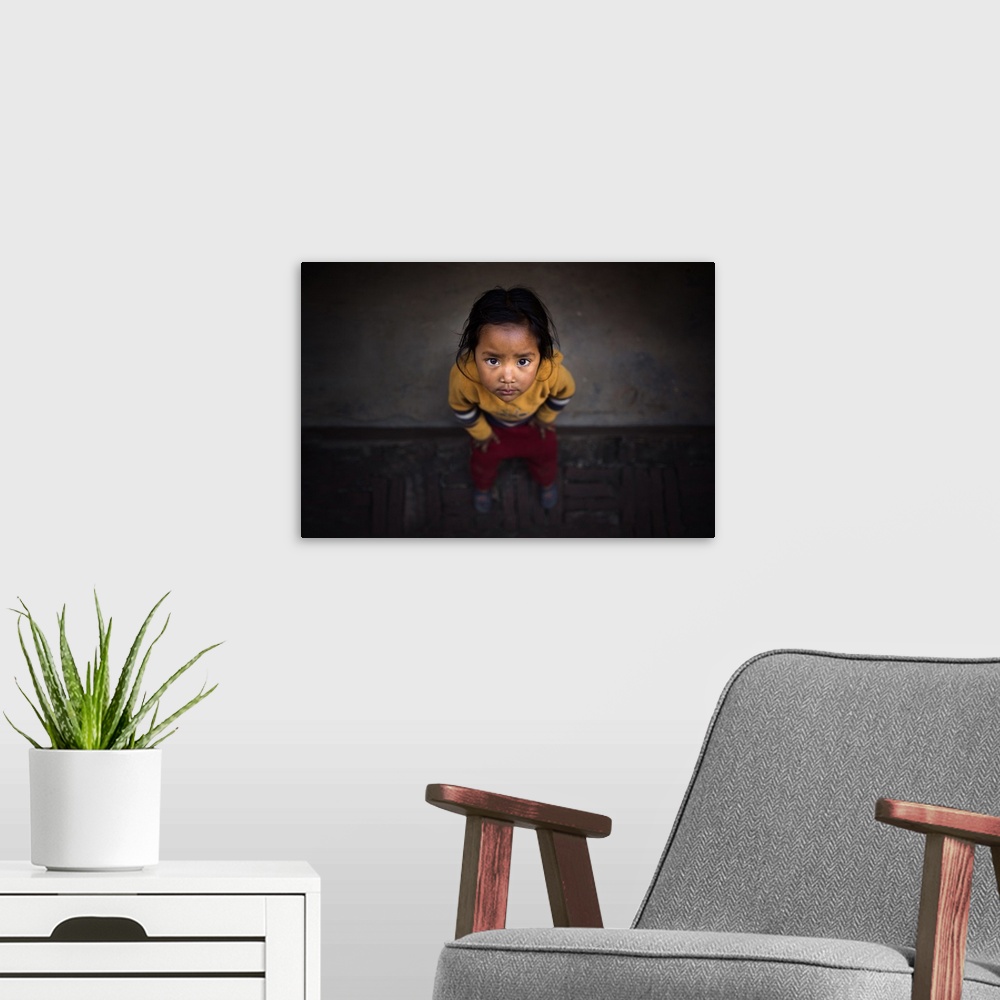 A modern room featuring A young Nepalese girl looking up with large dark eyes.