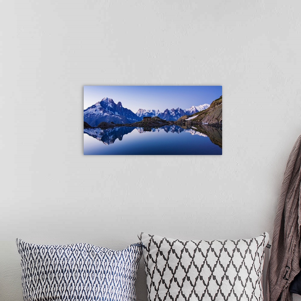 A bohemian room featuring A panoramic view of a blue mountain range with a crystal blue lake at the base reflecting the range.