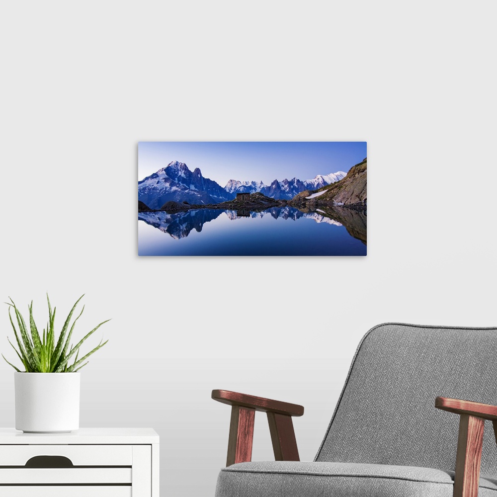 A modern room featuring A panoramic view of a blue mountain range with a crystal blue lake at the base reflecting the range.