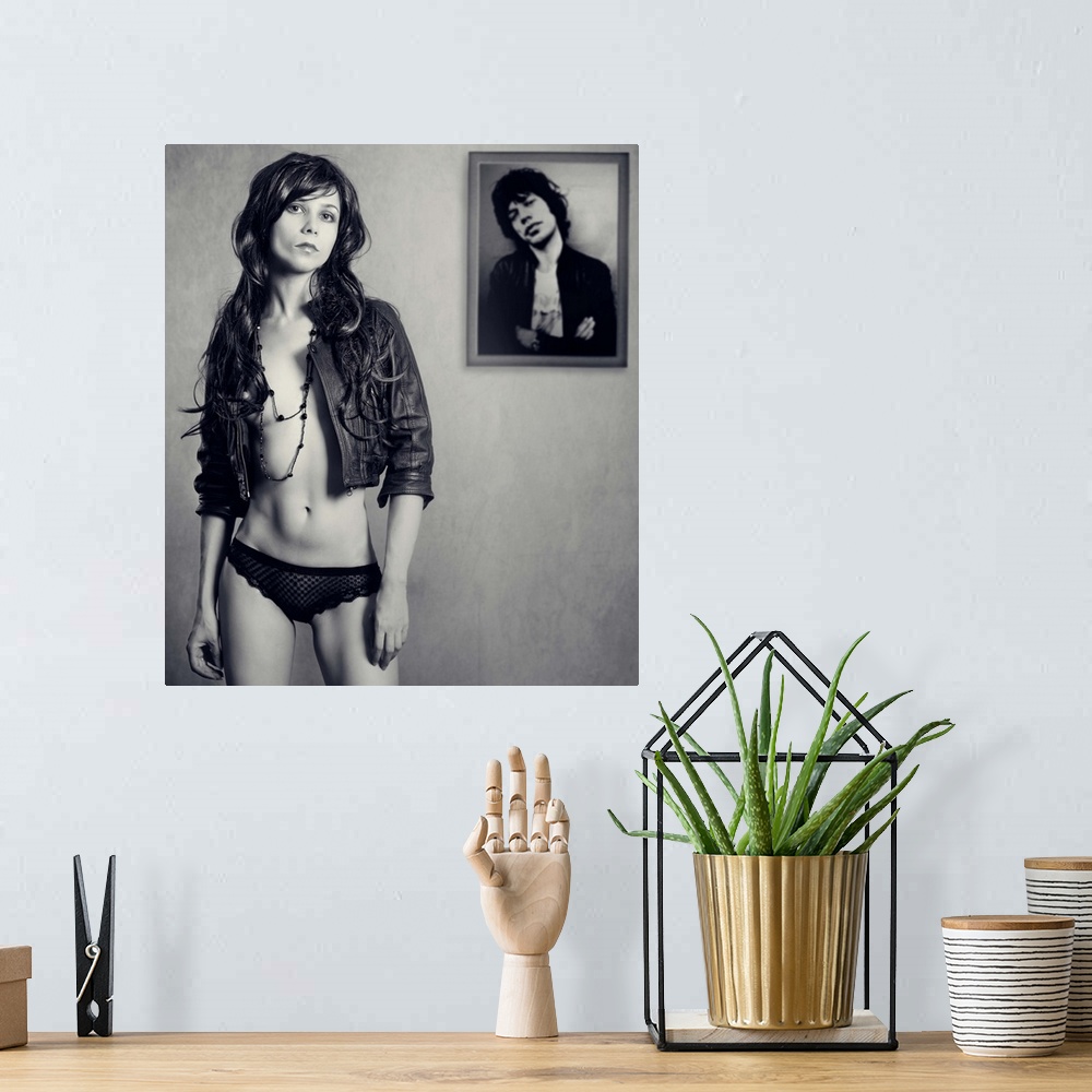 A bohemian room featuring A young woman wearing a leather jacket standing in front of a framed photo.