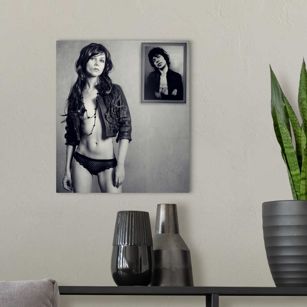 A modern room featuring A young woman wearing a leather jacket standing in front of a framed photo.
