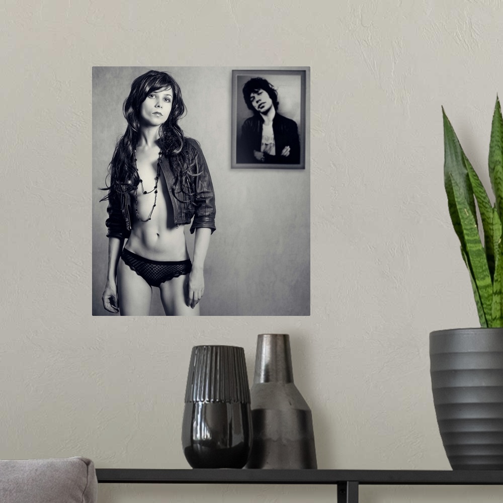 A modern room featuring A young woman wearing a leather jacket standing in front of a framed photo.