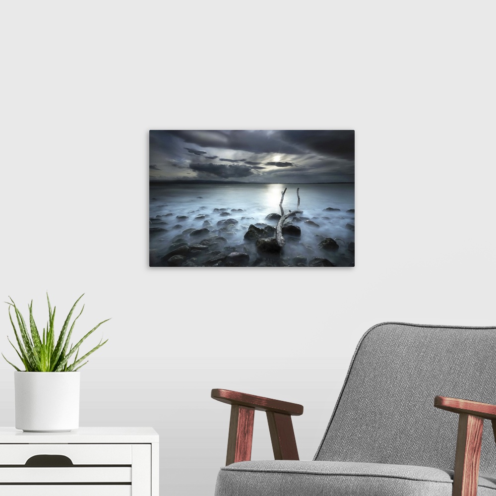 A modern room featuring Sun shining through dark clouds onto a misty lake, seen from the rocky shore.