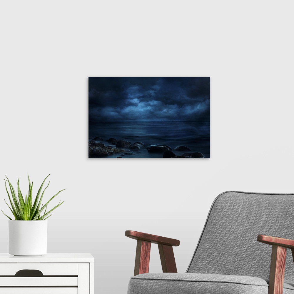 A modern room featuring Blue landscape photograph of a rocky seashore lit by moonlight with a bridge in the far distance.