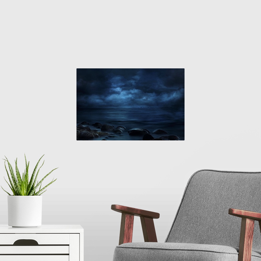 A modern room featuring Blue landscape photograph of a rocky seashore lit by moonlight with a bridge in the far distance.