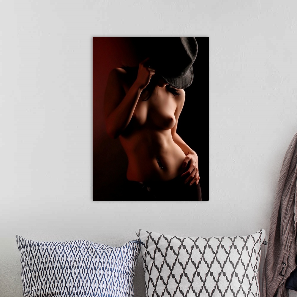 A bohemian room featuring A portrait of a nude woman cast in dynamic shadow with a hat covering her face.