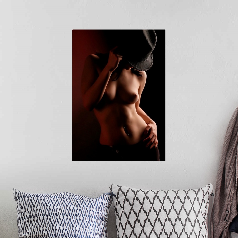 A bohemian room featuring A portrait of a nude woman cast in dynamic shadow with a hat covering her face.