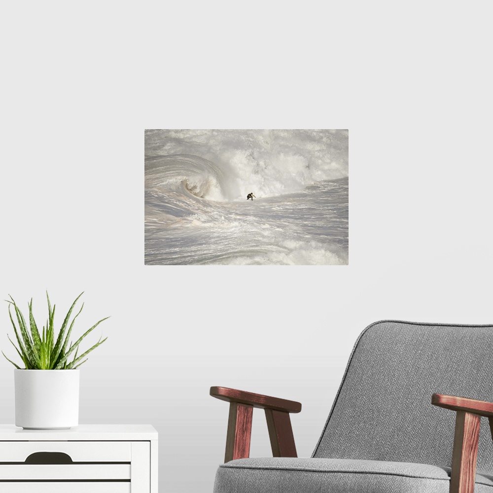 A modern room featuring A man on a surfboard riding rough looking white waves in vast ocean.