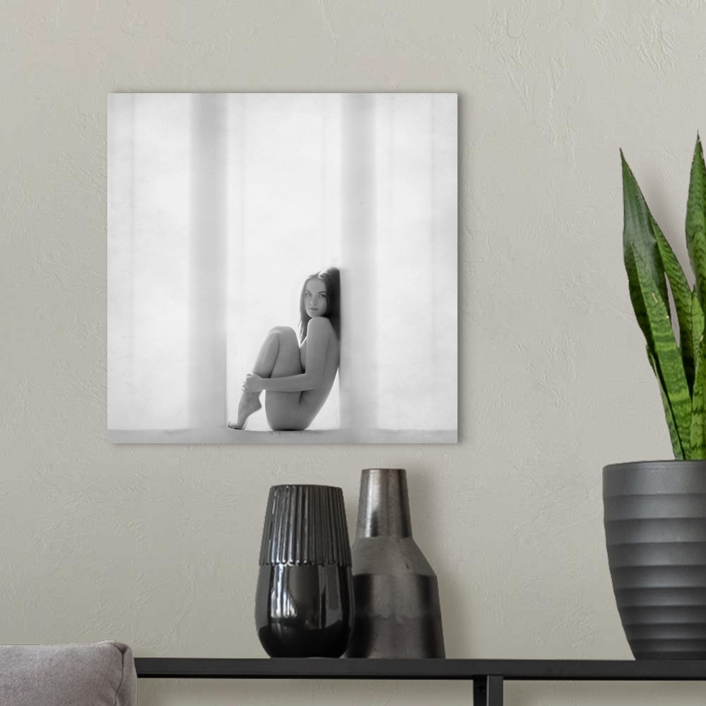 A modern room featuring Nude woman curled up in a window frame in black and white.