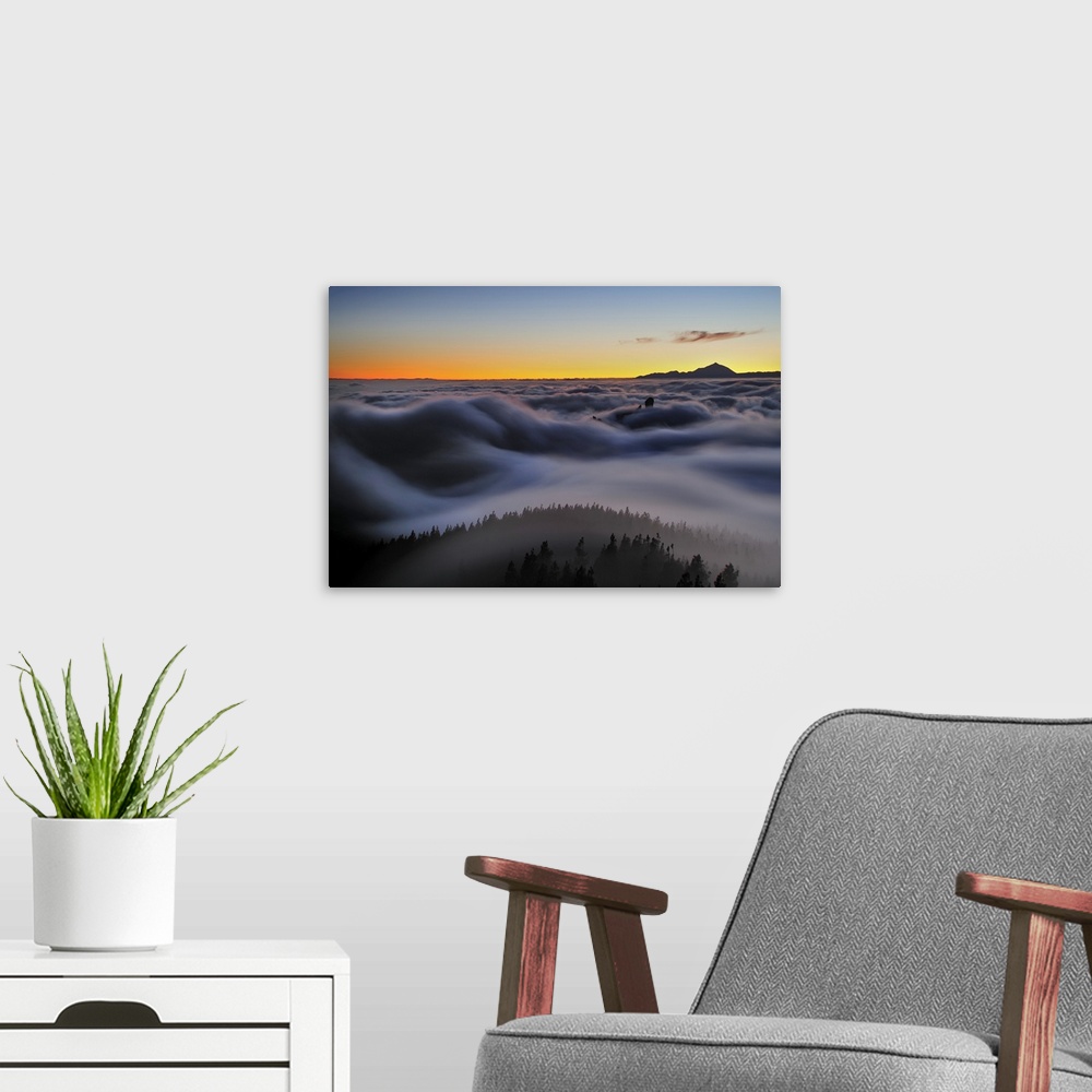 A modern room featuring A valley full of low clouds at sunset resembles a seascape, with a mountain in the distance.