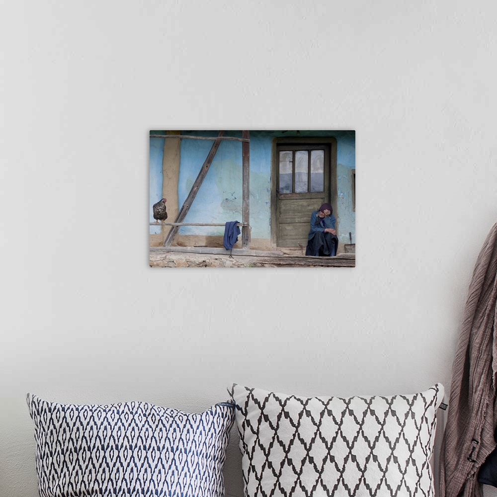 A bohemian room featuring Portrait of an old woman sitting on the doorstep of a blue house looking at a chicken.