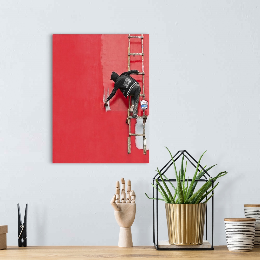 A bohemian room featuring A person hanging from a ladder, painting the side of a building bright red.