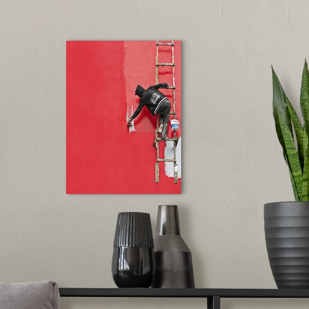 A modern room featuring A person hanging from a ladder, painting the side of a building bright red.