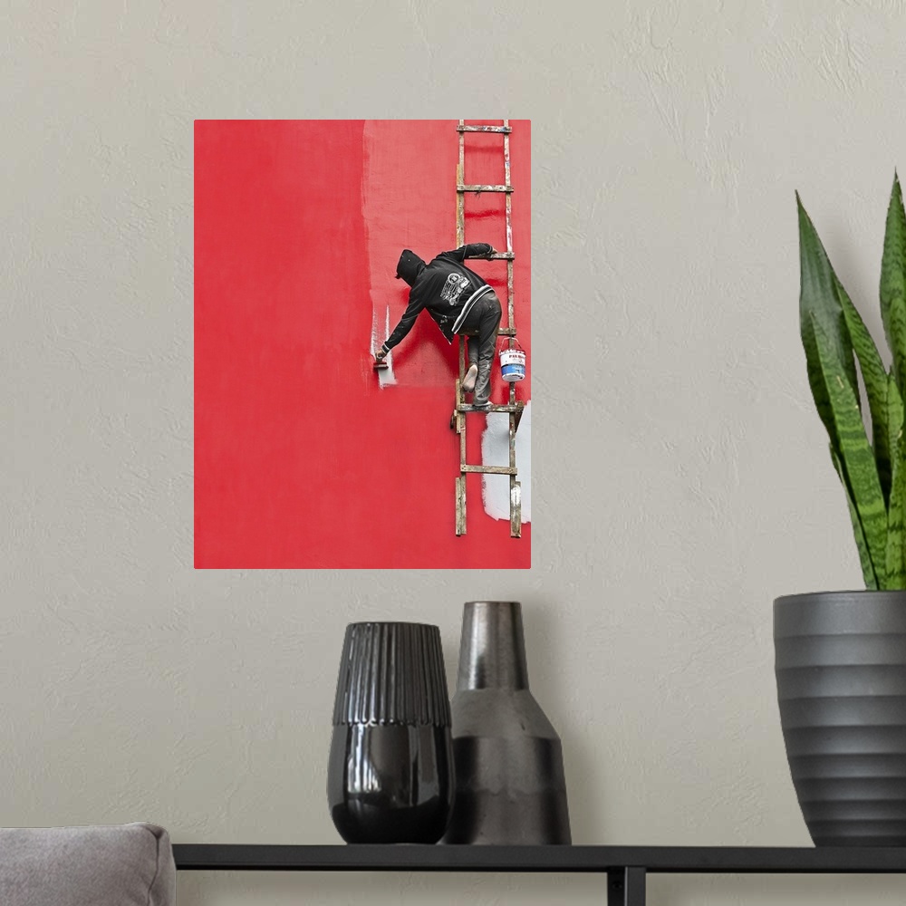 A modern room featuring A person hanging from a ladder, painting the side of a building bright red.