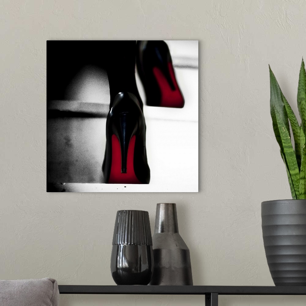 A modern room featuring Close up view of two black high heels with red soles walking up steps.